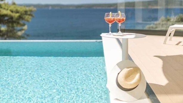 A poolside area with a clear view of the sea, two glasses of red drink, and a straw hat on the edge of the pool. - Villa Gelos by Villas Hvar (Zavala)