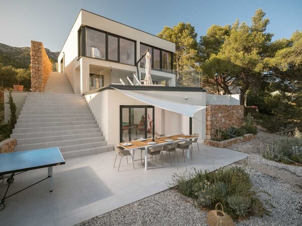 Una casa moderna con una escalera que lleva a un segundo piso, un comedor con mesa y sillas, y una mesa de ping-pong.