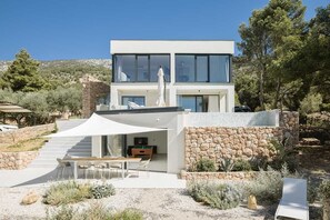 Una casa moderna de dos plantas con fachada de piedra, un porche cubierto con mobiliario exterior y vistas del paisaje circundante.