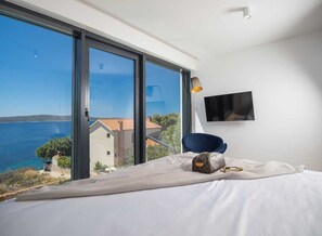 Un dormitorio con un ventanal grande, una cama, una silla, un televisor y una lámpara.
