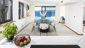 A modern dining area with a round table, white chairs, a potted plant, and a fruit bowl. - Villa Gelos by Villas Hvar (Zavala)