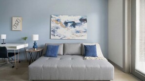 A modern living room with a grey sofa, two blue pillows, a white side table, a blue lamp, and a framed abstract painting on the wall. - Landing | Amazing 1BD, Pool, Gym (Nashville)