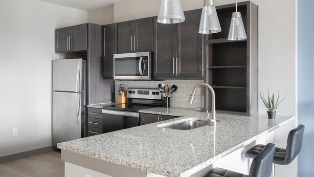 Una cocina moderna con armarios oscuros, electrodomésticos de acero inoxidable, encimera de granito e iluminación colgante.