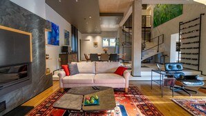 Un salon moderne avec un canapé, une table basse et un téléviseur. Un escalier mène à un autre niveau.