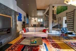 Een moderne woonkamer met een bank, salontafel en televisie. Een trap leidt naar een ander niveau.