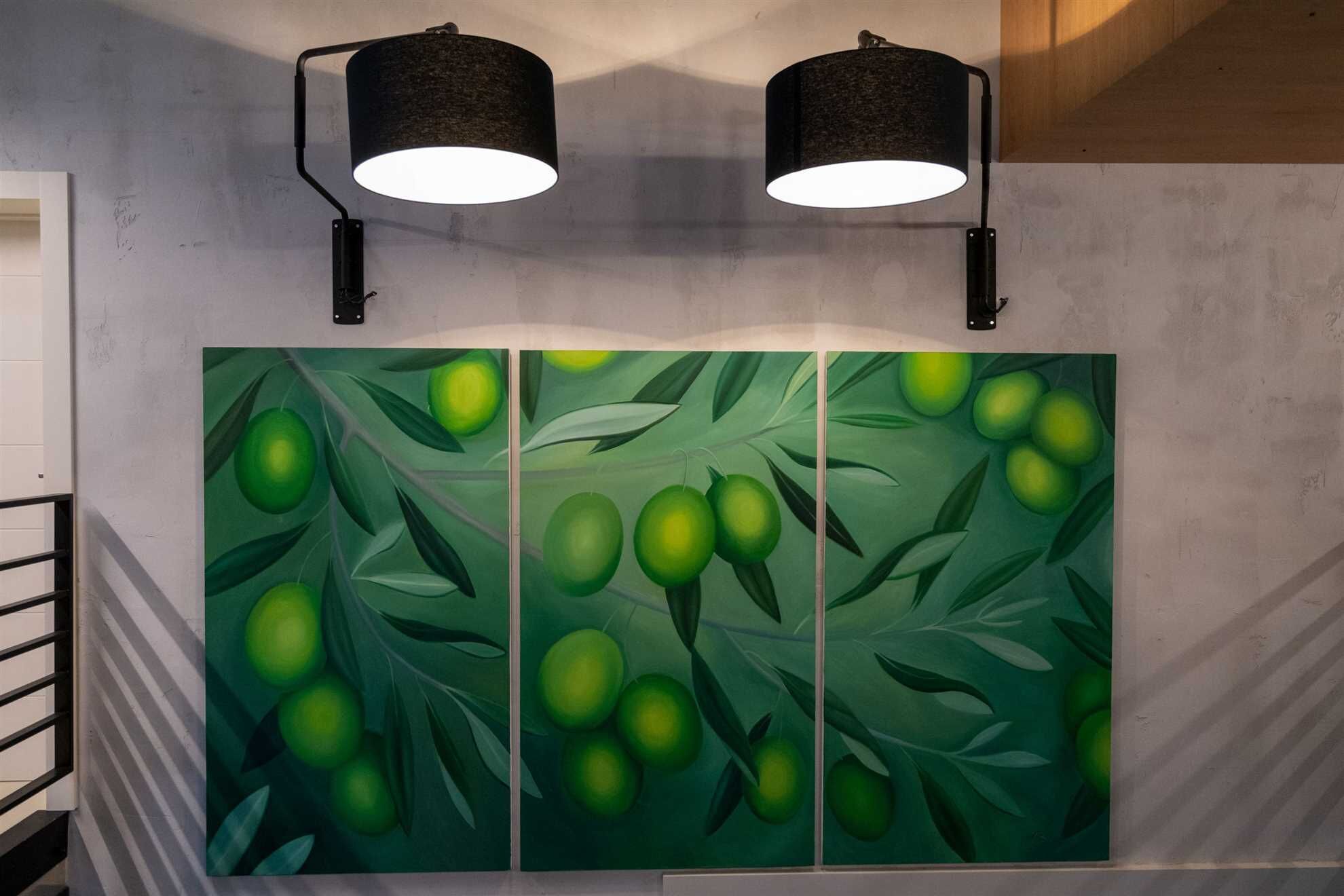 A wall with a large green fruit painting and two black wall-mounted lamps.