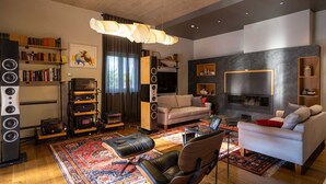 Un salon moderne avec un canapé, une table basse, un téléviseur et une cheminée. On y trouve également des étagères et un tapis.