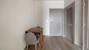 Una stanza piccola con un tavolo di legno e una sedia, una porta chiusa e una finestra con persiane.