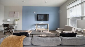 Ein modernes Wohnzimmer mit einer Couch, einem Couchtisch, einem Fernseher und einem Schreibtisch mit einer Lampe.