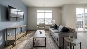 Ein modernes Wohnzimmer mit Flachbildfernseher, einer Couch, einem Couchtisch und einem kleinen Beistelltisch mit Pflanze.