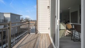 Un balcone con pavimento in legno, una porta scorrevole in vetro che dà su un angolo cottura con un bancone e due sedie.