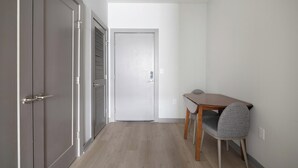 Un corridoio con un tavolo in legno e una sedia grigia, una porta chiusa e un muro con l'interruttore della luce.