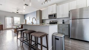 A modern kitchen with white cabinets, stainless steel appliances, and a bar area with stools.