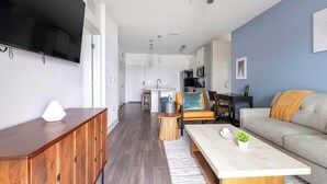 Un salon moderne avec un canapé, une table basse et un téléviseur. Il y a également un coin cuisine avec une table à manger et des chaises.