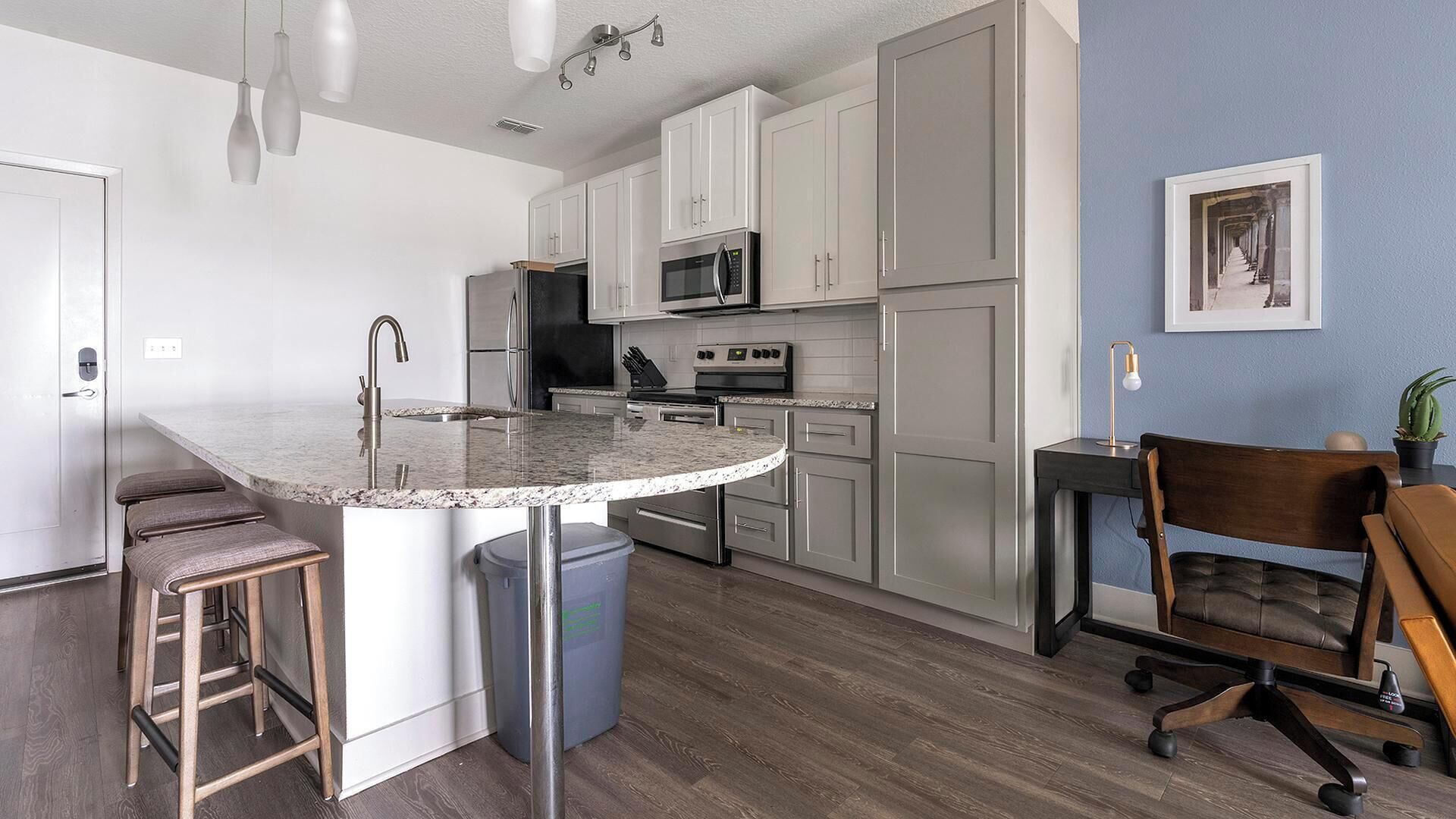 A modern kitchen with white cabinets, a granite countertop, stainless steel appliances, and a dining area with a wooden chair and bar stools.