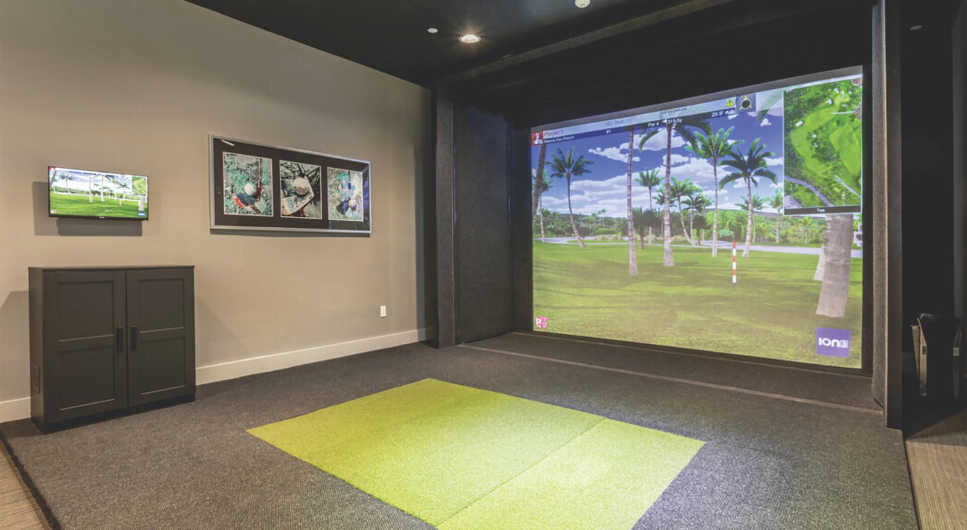A room with a large screen displaying a golf game, a flat-screen TV, framed artwork, and a carpeted floor.