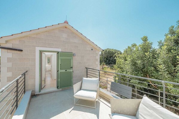 Ein kleines Gebäude mit Tür und Fenster, ein Balkon mit Geländer und ein Stuhl.