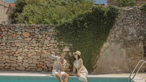 A poolside area with a stone wall, a wooden table with drinks and snacks, and a lounge chair. - Villa Lesina by Villas Hvar (Vrboska)