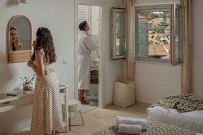 Ein Schlafzimmer mit einem Bett, einem Spiegel, einer Kommode und einem Fenster mit Blick auf Gebäude.