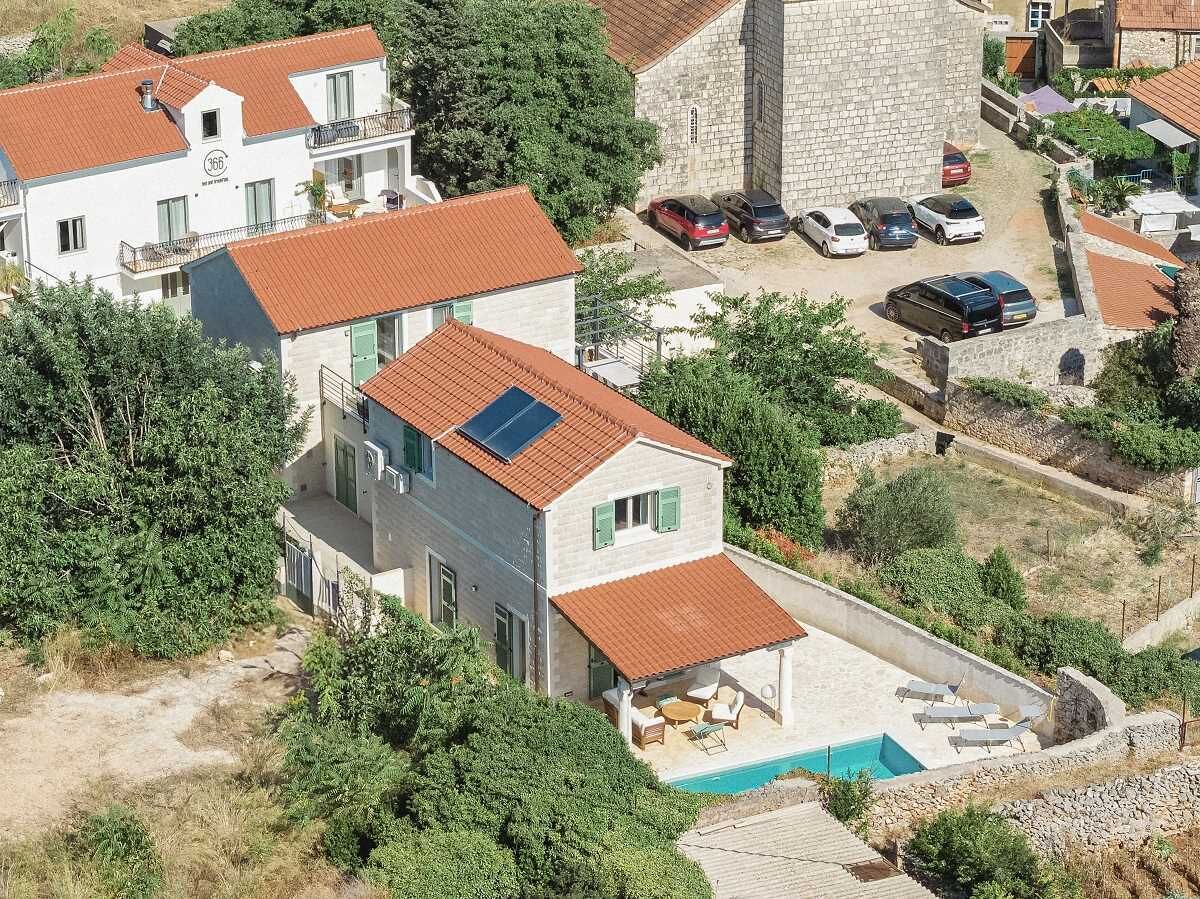 A two-story house with a swimming pool, a stone tower, and a parking area with multiple cars.