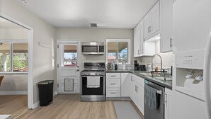 A modern kitchen with stainless steel appliances, white cabinetry, and a view through the window. - Sleeps 12 · Game Room · Foosball · Yard BBQ · 3BR Near Anschutz & Denver (Aurora)