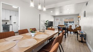 A modern kitchen with white cabinets, a dining area with a wooden table and brown chairs, and a living area with a sofa and a coffee table. - Sleeps 12 · Game Room · Foosball · Yard BBQ · 3BR Near Anschutz & Denver (Aurora)