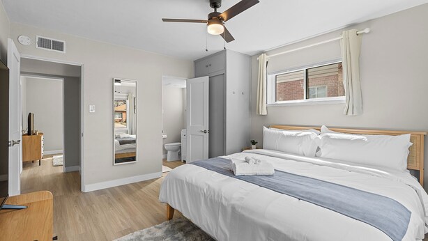 A bedroom with a bed, a ceiling fan, a window with curtains, a wooden floor, and a door leading to another room. - Sleeps 12 · Game Room · Foosball · Yard BBQ · 3BR Near Anschutz & Denver (Aurora)