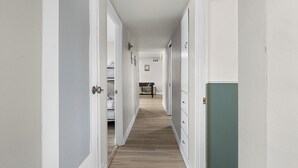 A narrow hallway with white walls and wooden flooring, leading to a room with a bed and a desk. - Sleeps 12 · Game Room · Foosball · Yard BBQ · 3BR Near Anschutz & Denver (Aurora)