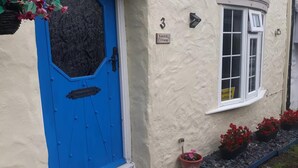 A cottage with a blue door, a window with a sign, and potted plants. - Bumble Cottage - Parking - Pet - Garden - Sleeps 4 (Ilfracombe)