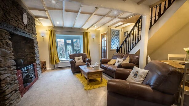 A cozy living room with a stone fireplace, leather sofas, a wooden coffee table, and a staircase. - Bumble Cottage - Parking - Pet - Garden - Sleeps 4 (Ilfracombe)