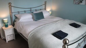 A neatly made bed with a headboard, two bedside lamps, a small bedside table, and a wall decoration. - Bumble Cottage - Parking - Pet - Garden - Sleeps 4 (Ilfracombe)