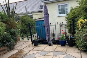 Ein Garten mit einem Kiesweg, einem blauen Tor und Kübelpflanzen.