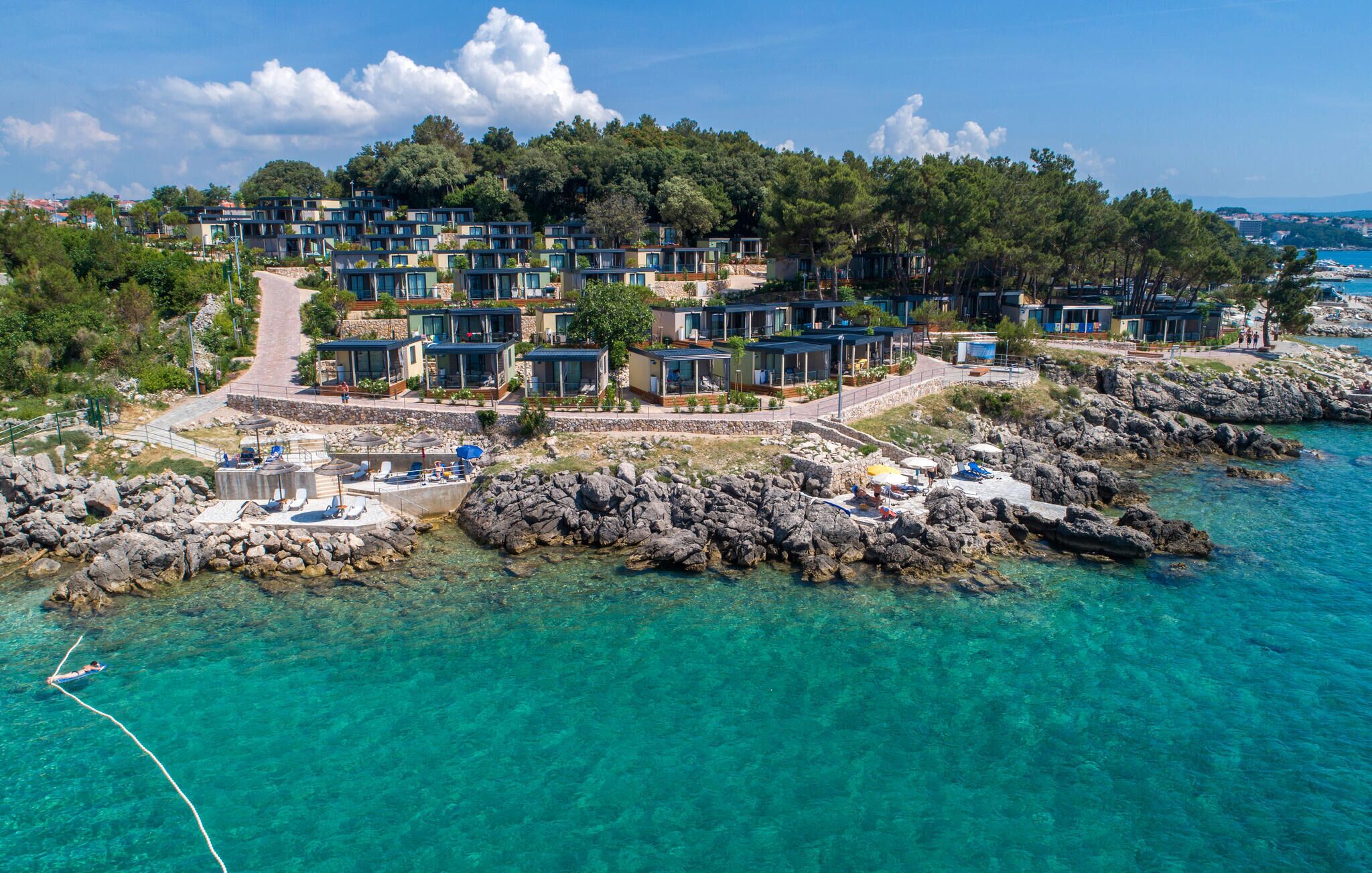 Een kustresort met moderne villa's, helder turquoise water en rotsachtig terrein.