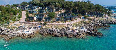 Een kustresort met moderne villa's, helder turquoise water en rotsachtig terrein.