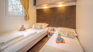 A twin room with two beds, a window with curtains, a small bedside table, and a headboard with built-in lighting.