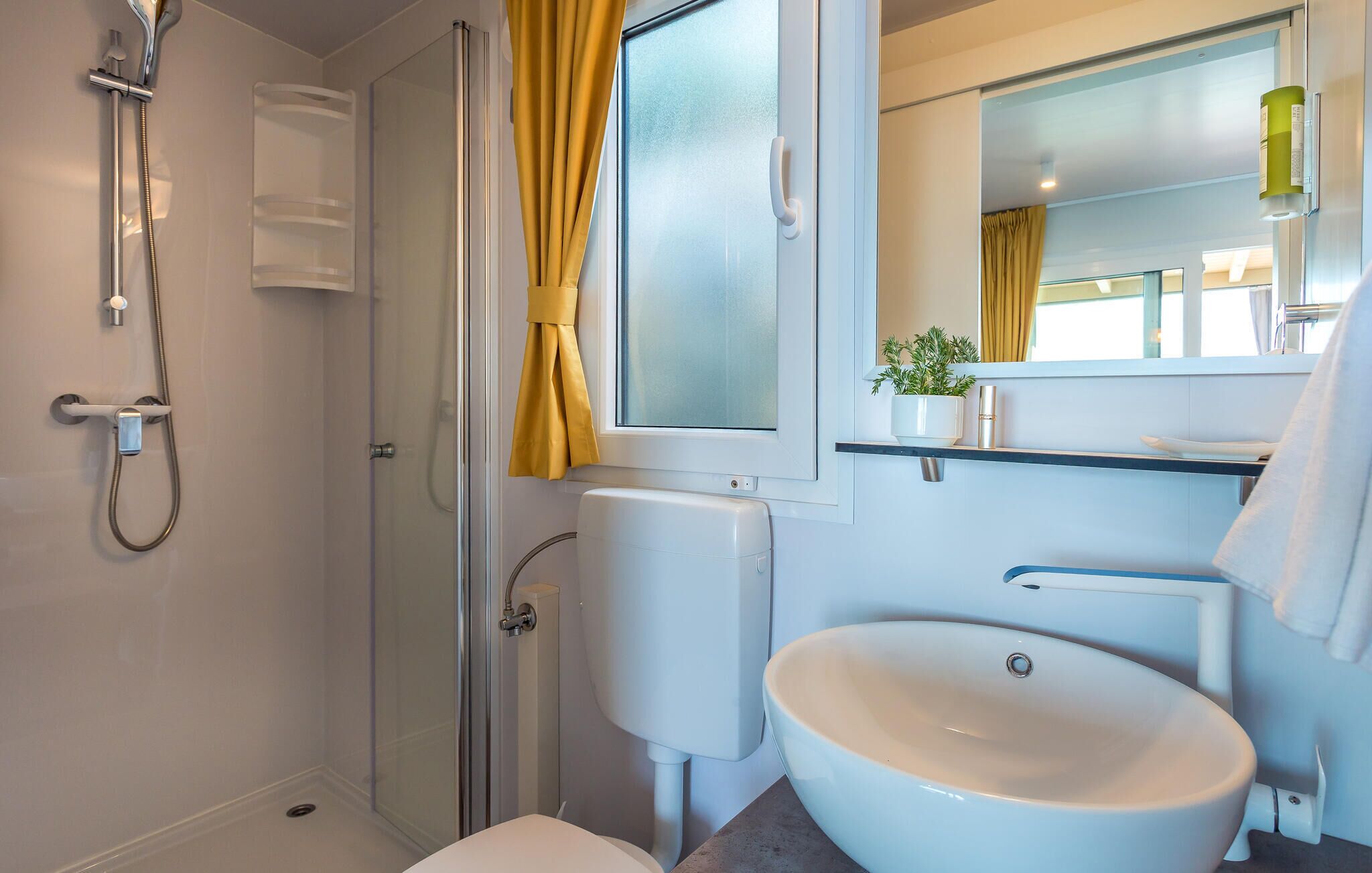 Een badkamer met douche, toilet, wastafel en een raam met gordijnen.