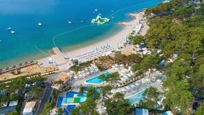 An aerial view of a coastal resort with a beach, a swimming pool, and several boats in the water.