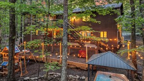 Een houten chalet met een terras, omgeven door bomen, en lichtjes.