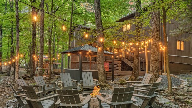 Een bebost buitengebied met een vuurkuil, Adirondack-stoelen en lichtslingers.