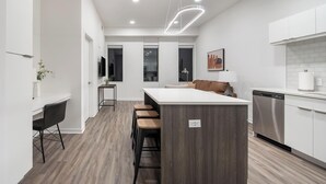 Una cocina moderna con una isla central, taburetes de bar, zona de comedor y lavavajillas integrado.