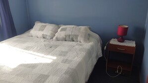 A bed with a quilt, two pillows, a nightstand with a lamp, and a power outlet. - C1 Furnished Cabin Near downtown Puerto Montt (Puerto Montt)