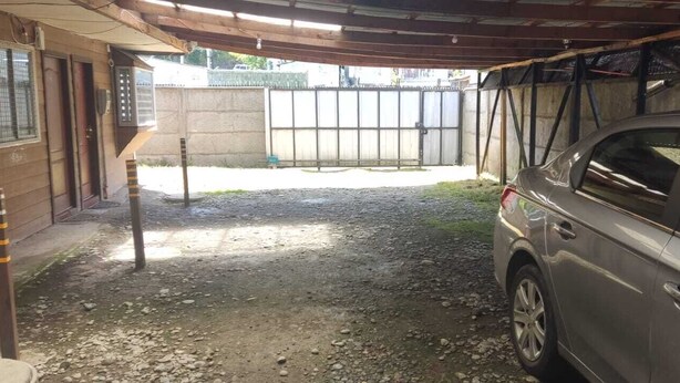 A covered outdoor area with a gravel path, a parked car, and a metal gate. - C1 Furnished Cabin Near downtown Puerto Montt (Puerto Montt)