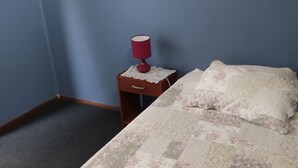 A small bedroom with a single bed, a nightstand with a lamp, and a wooden drawer. - C1 Furnished Cabin Near downtown Puerto Montt (Puerto Montt)