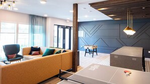 Moderni hotellihuone, jossa on sohva, pöytäjalkapallopeli, pingispöytä ja suuri ikkuna.