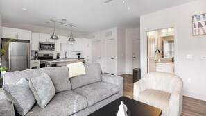 Ein modernes Wohnzimmer mit einem grauen Sofa, einem weißen Sessel, einem schwarzen Couchtisch und einer Küche im Hintergrund.