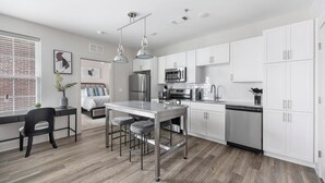 A modern kitchen with white cabinets, stainless steel appliances, and a bar area with stools. - Landing | Modern 2BD, Game Room, Courtyard (Richmond)