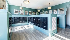 A room with a blue wall, a row of mailboxes, and a wooden floor. - Landing | Modern 2BD, Game Room, Courtyard (Richmond)