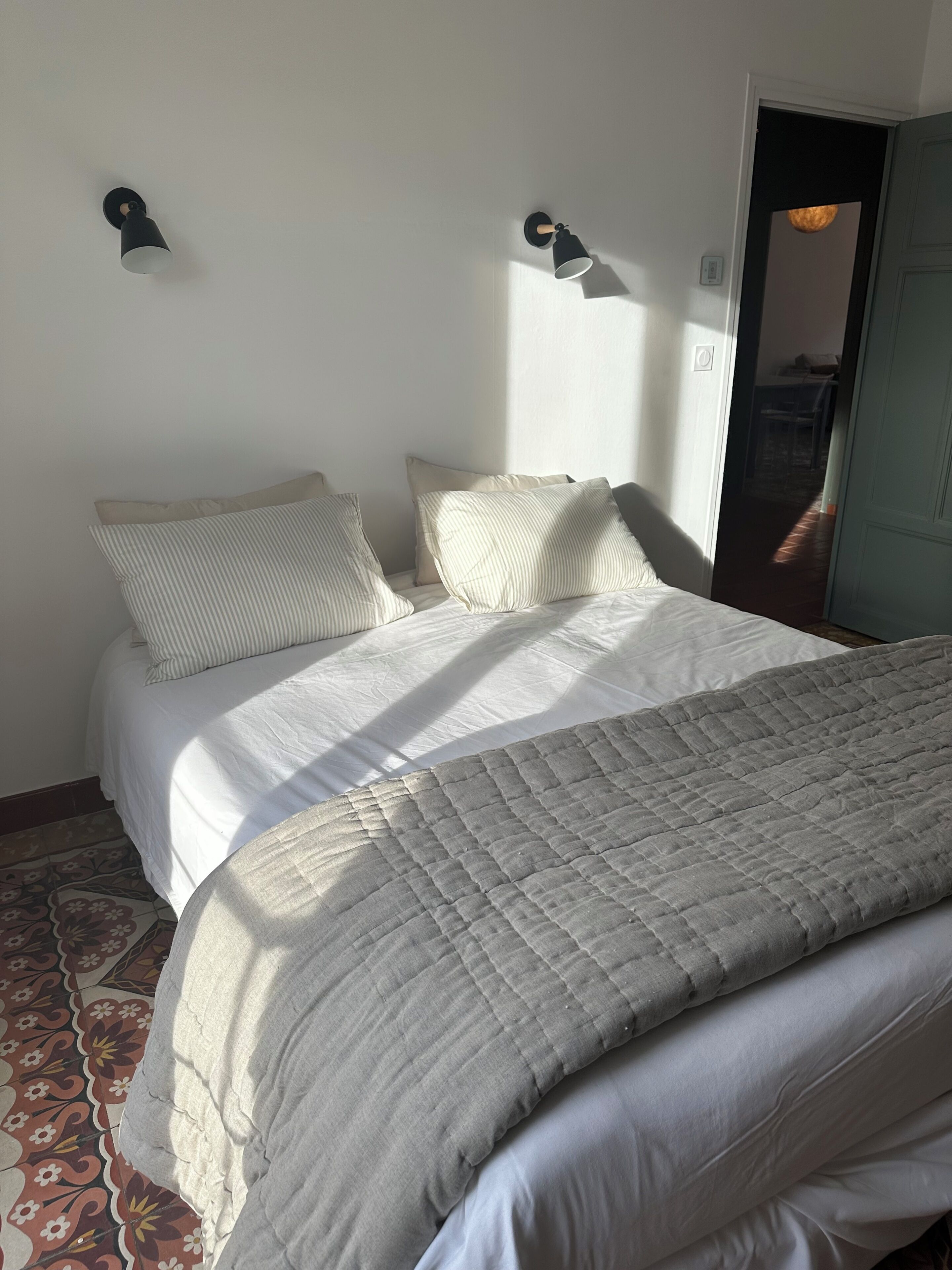Ein Schlafzimmer mit einem Bett, Kissen, einer gesteppten Decke, einer Wandleuchte und einer Tür.