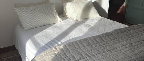 Ein Schlafzimmer mit einem Bett, Kissen, einer gesteppten Decke, einer Wandleuchte und einer Tür.