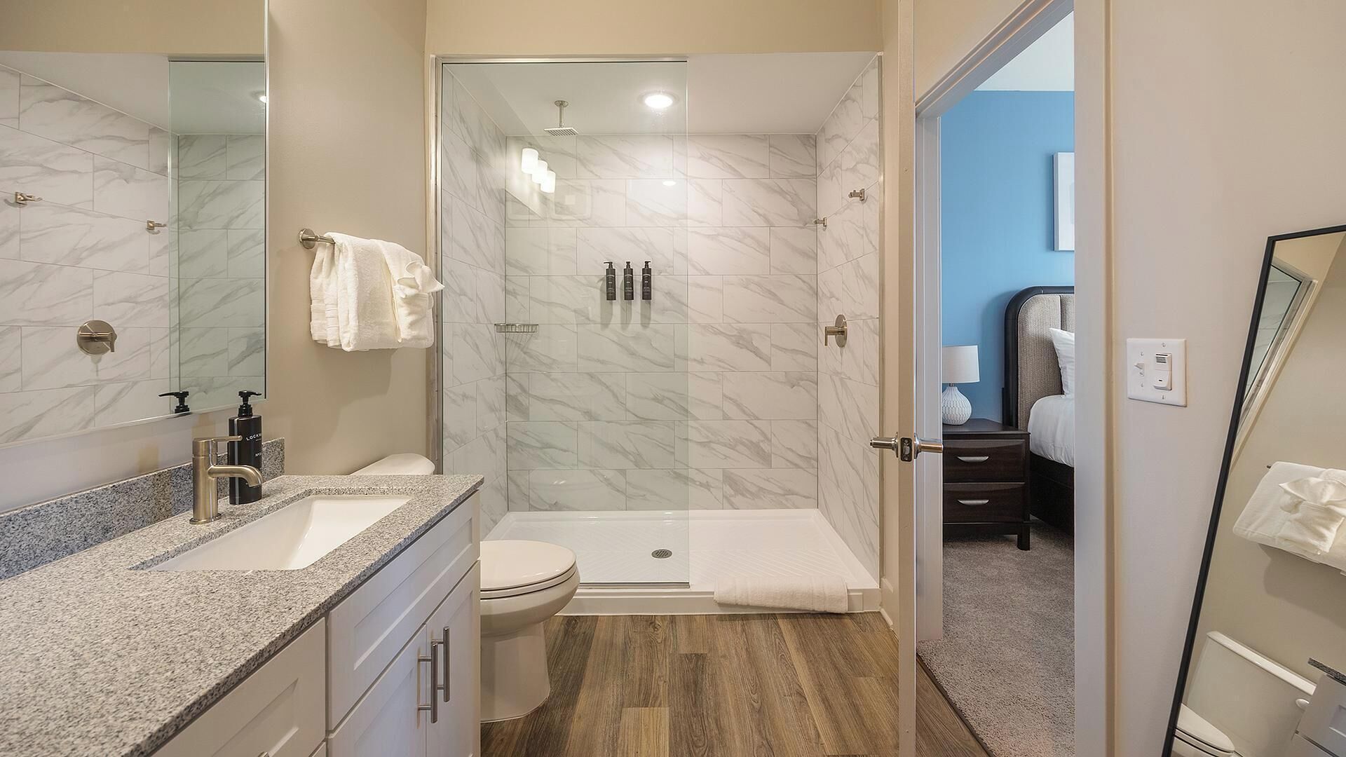 A modern bathroom with a shower, toilet, and sink, marble tiles, and a wooden floor.